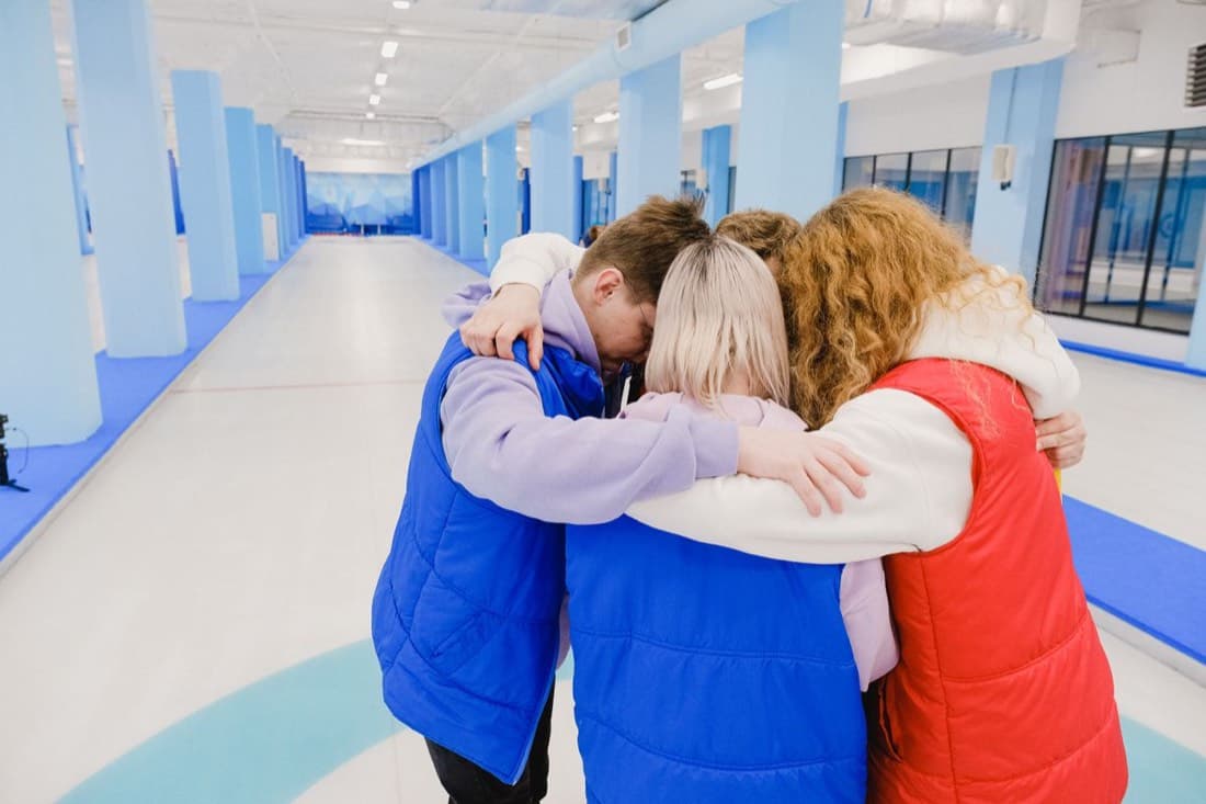 Four teammates in a huddle, arms around each other's backs, facing away from the camera